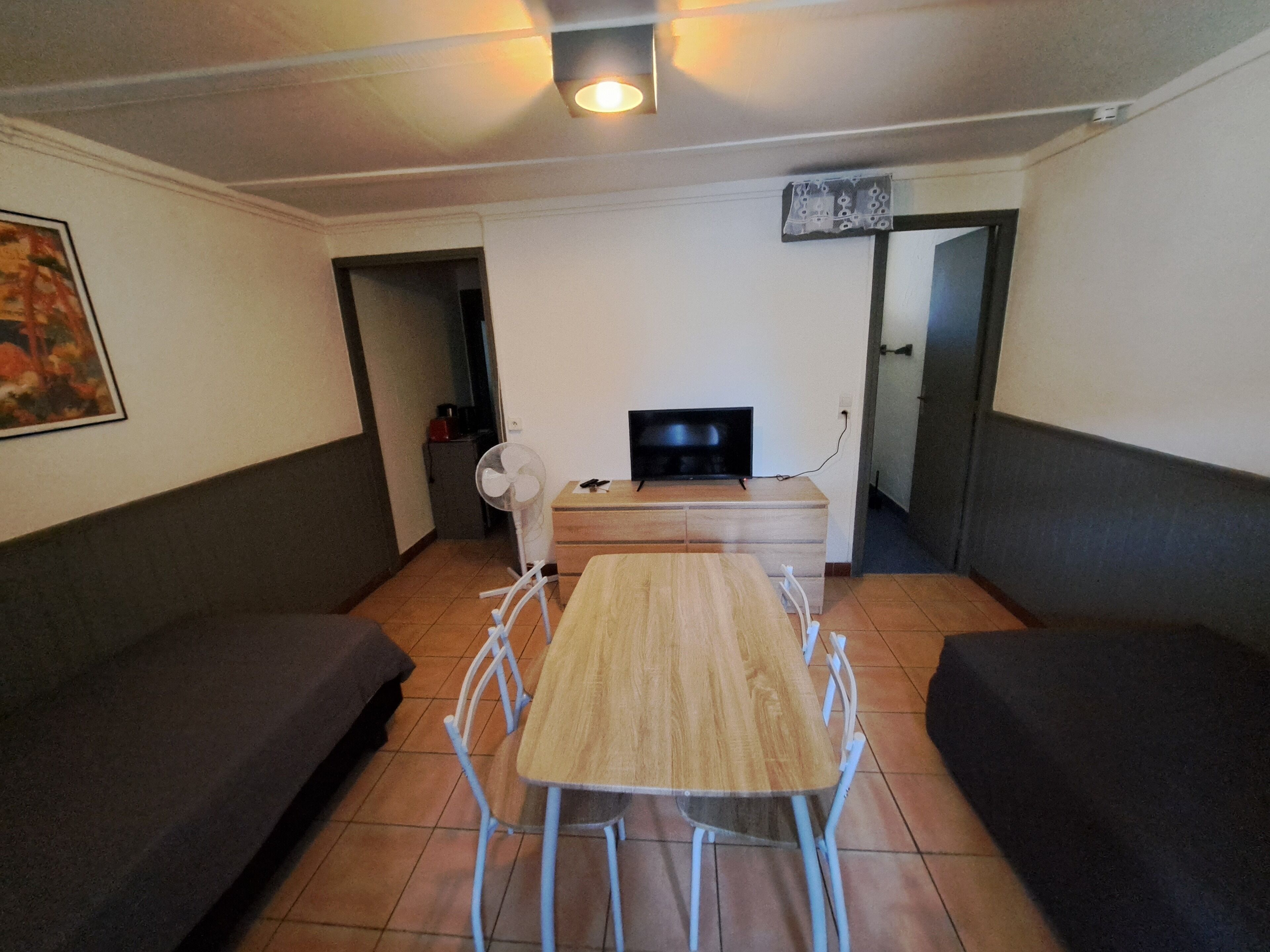 Ein Wohnzimmer mit einem Holztisch, zwei Sofas, einem Fernseher und einem Ventilator.