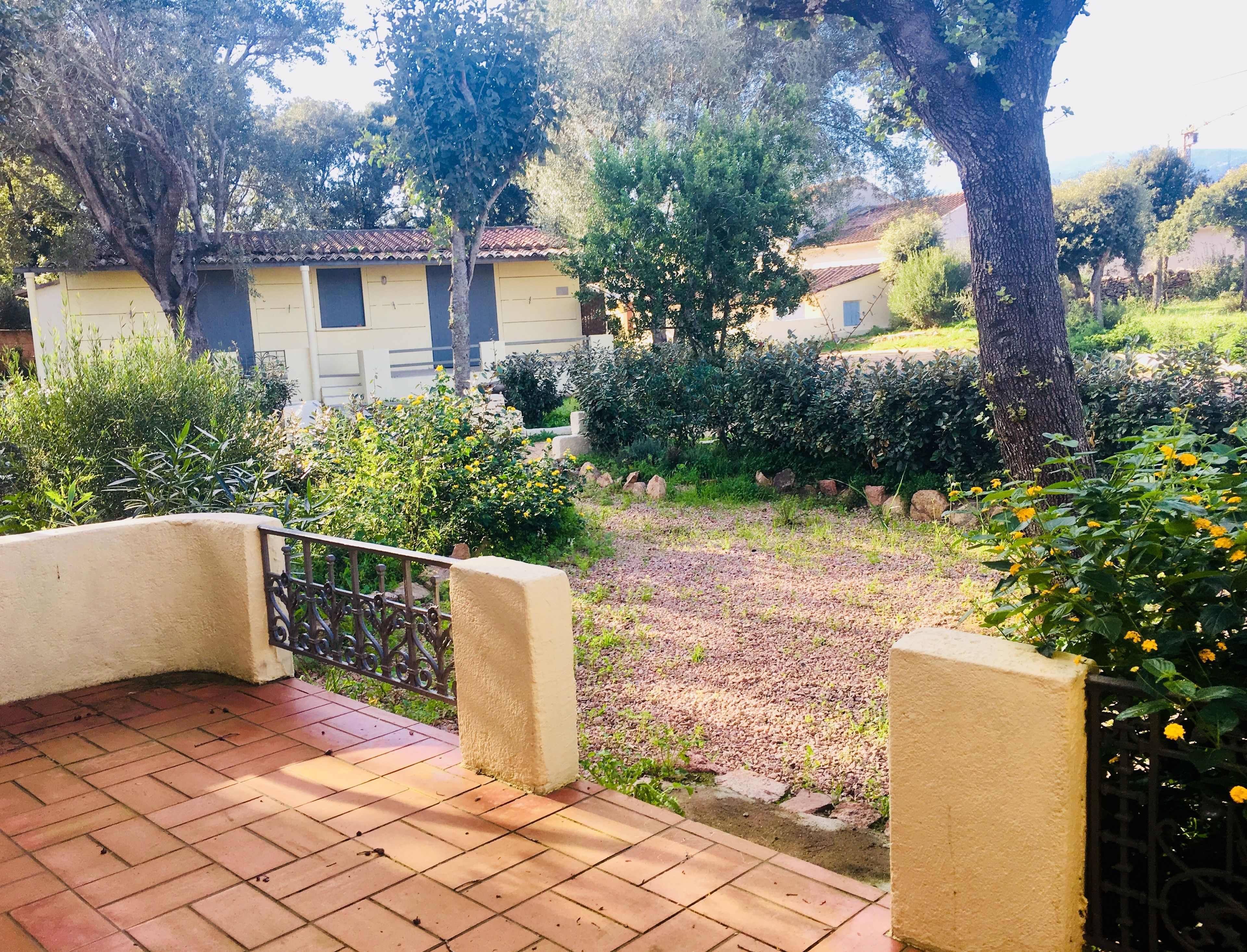 Una zona con patio, pavimento in piastrelle, ringhiera in metallo e vista su un edificio con tetto in tegole e parete gialla.