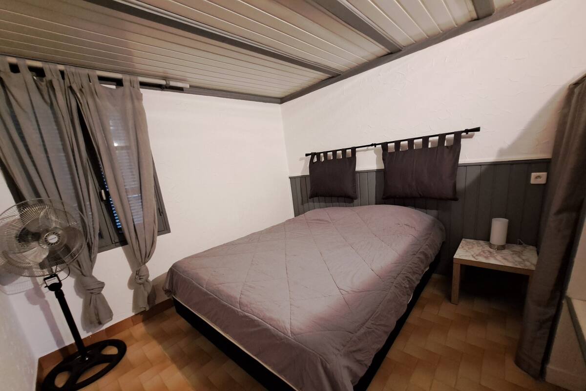Une chambre à coucher avec un lit, une table de chevet, un ventilateur et des rideaux.