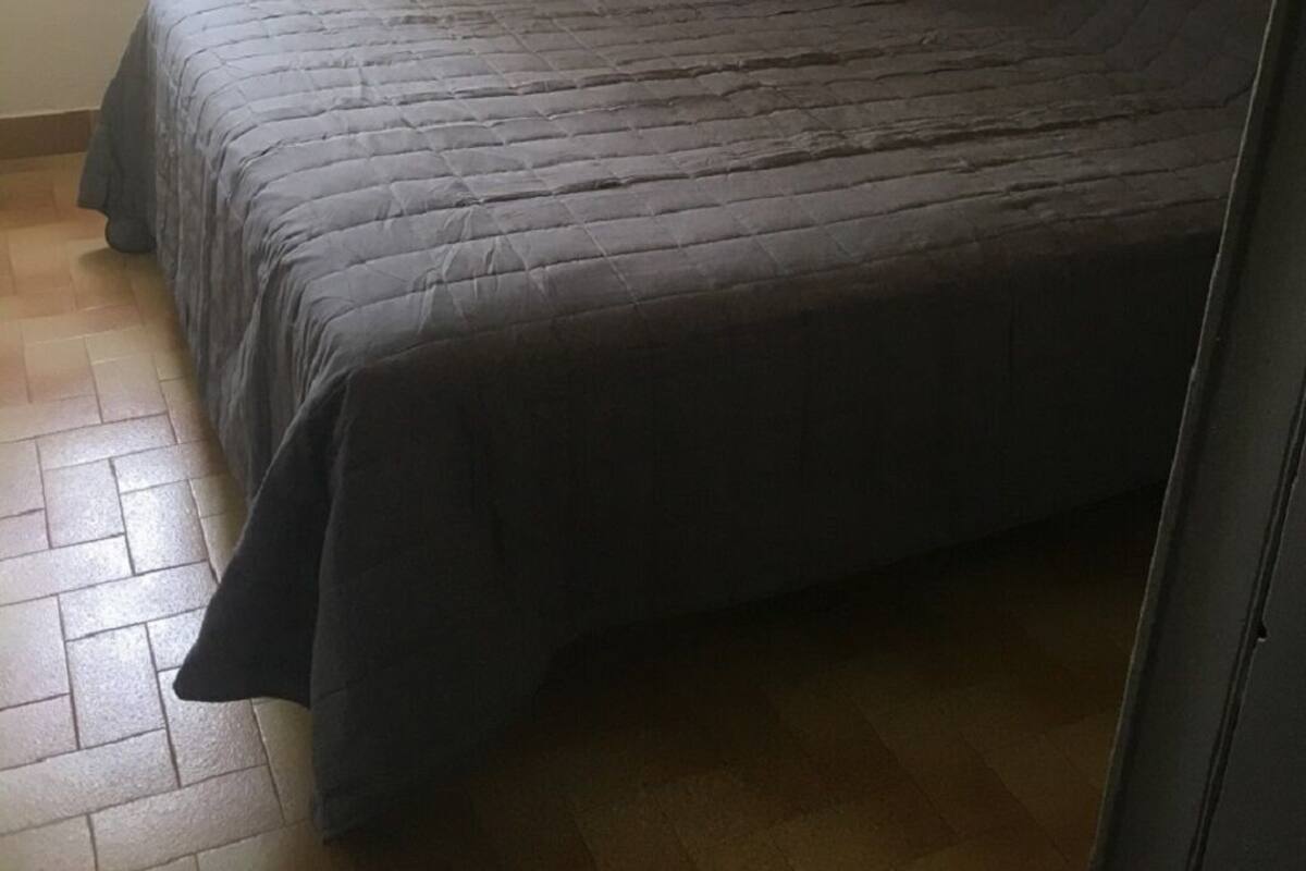 Une chambre à coucher avec un lit, une fenêtre avec des rideaux, un luminaire suspendu et un sol carrelé.