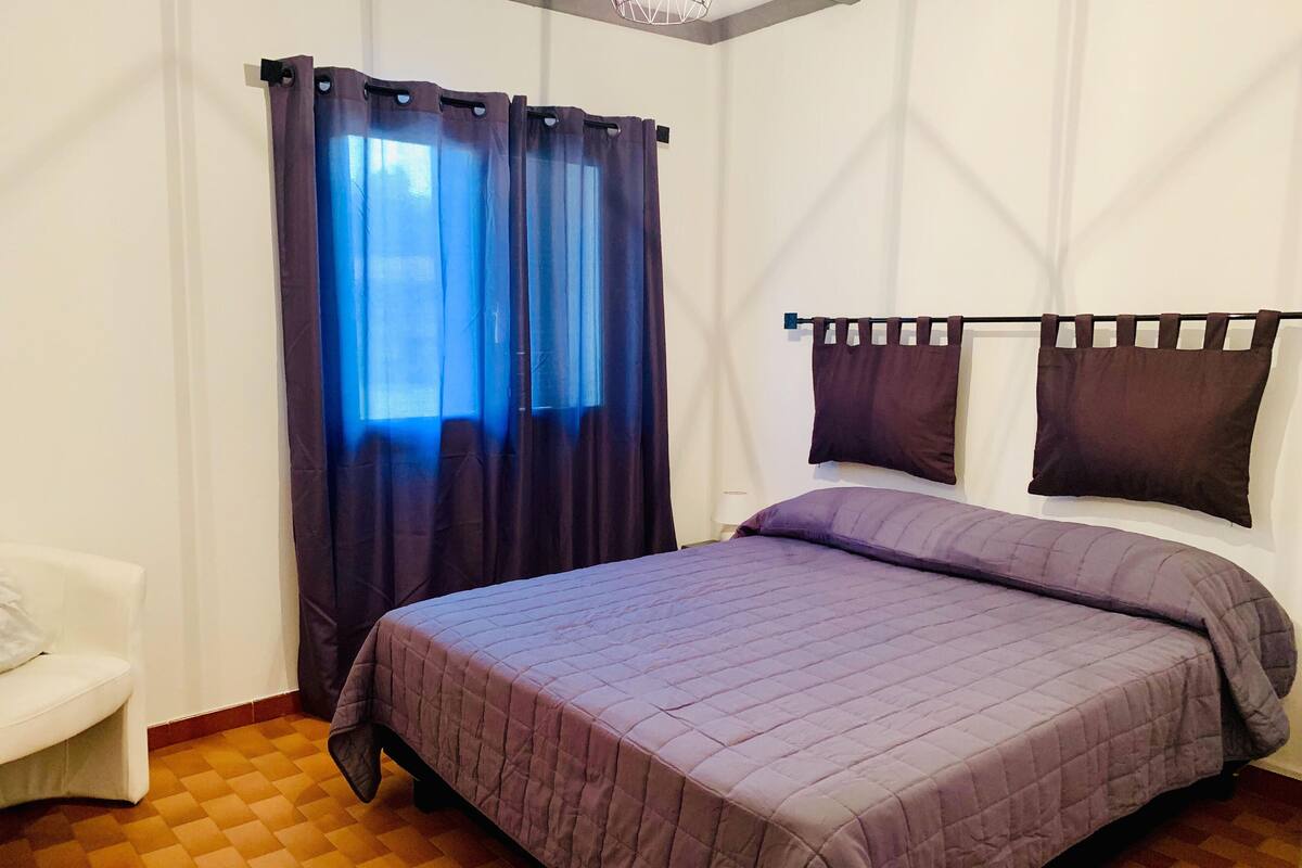 Une chambre à coucher avec un lit, des rideaux, une table de chevet et une chaise.