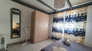 A bedroom with a bed, a wardrobe, a mirror, a standing fan, and a curtain with a nautical theme. - Résidence Filippi (Porto-Vecchio)