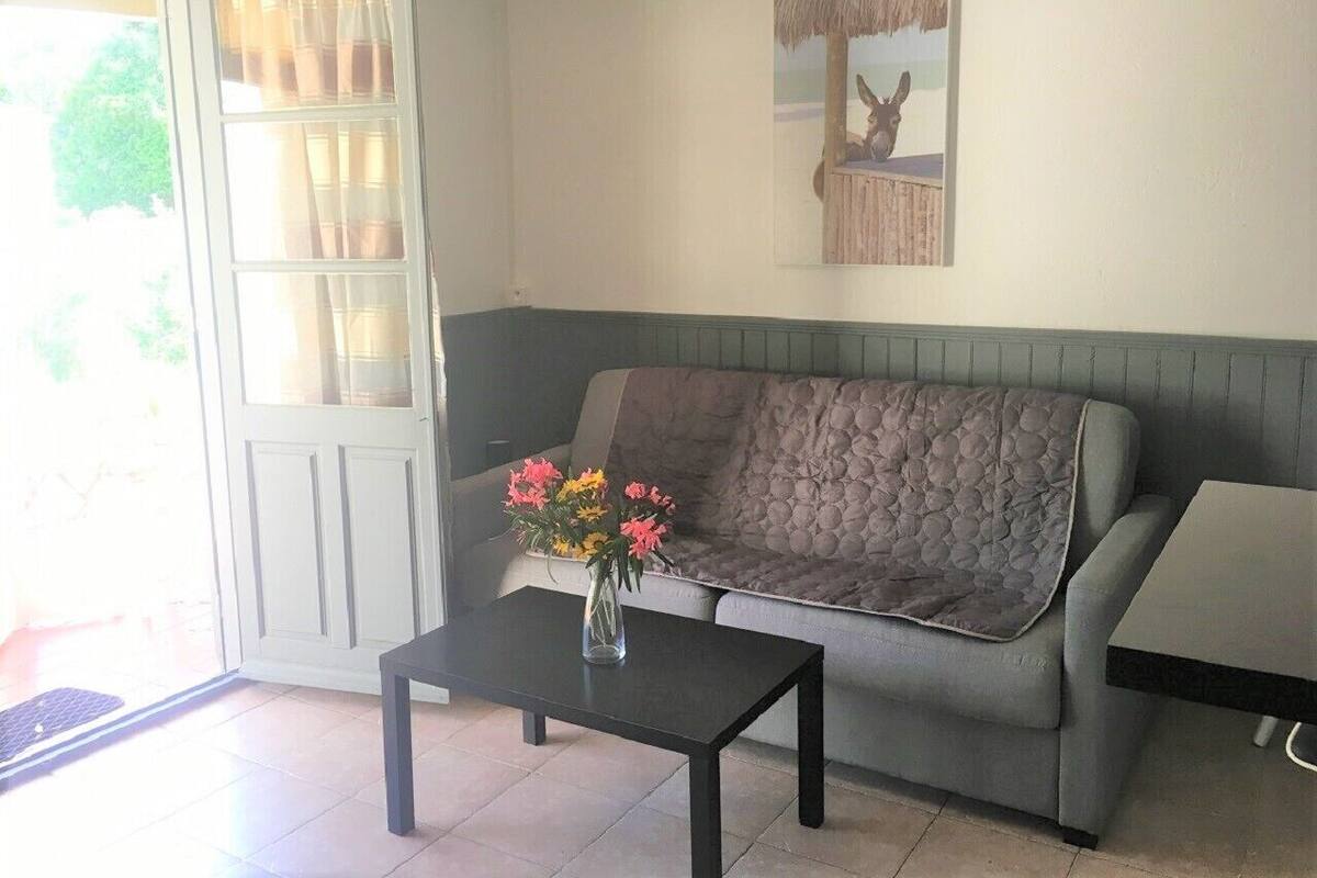 Un salon avec un canapé gris, une table basse noire ornée d’un vase de fleurs et une petite table accompagnée d’une chaise.