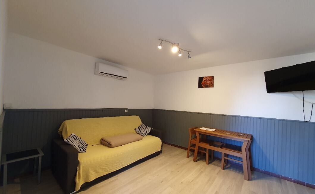 Ein Zimmer mit einem gelben Sofa, einer Holzbank, einem kleinen Tisch und einem an der Wand befestigten Fernseher.