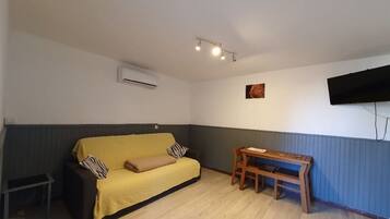 Ein Zimmer mit einem gelben Sofa, einer Holzbank, einem kleinen Tisch und einem an der Wand befestigten Fernseher.