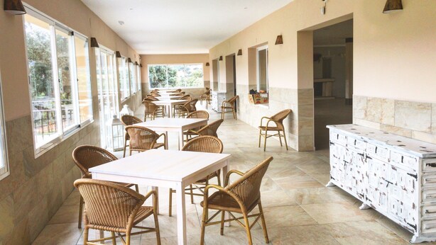 A spacious dining area with wicker chairs and white tables, large windows, and a marble floor. - Finca Encinar de las Flores (Los Navalucillos)