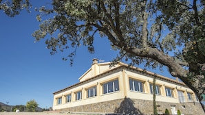 A two-story building with a stone facade and multiple windows. - Finca Encinar de las Flores (Los Navalucillos)