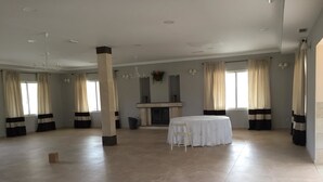 A spacious room with a round table and chairs, large windows with curtains, and a fireplace. - Finca Encinar de las Flores (Los Navalucillos)