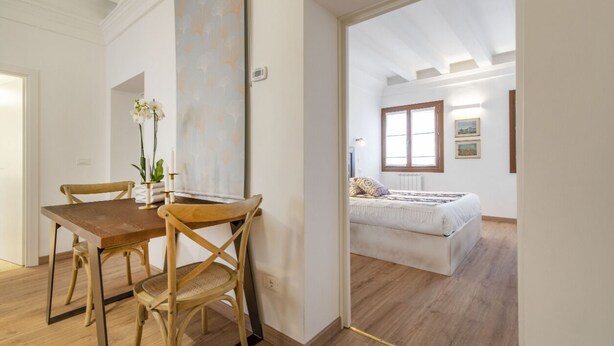 A room with a wooden dining table and chairs, a bed with a white duvet, and a painting on the wall. - San Marco Schiavoni Apartments (Venice)