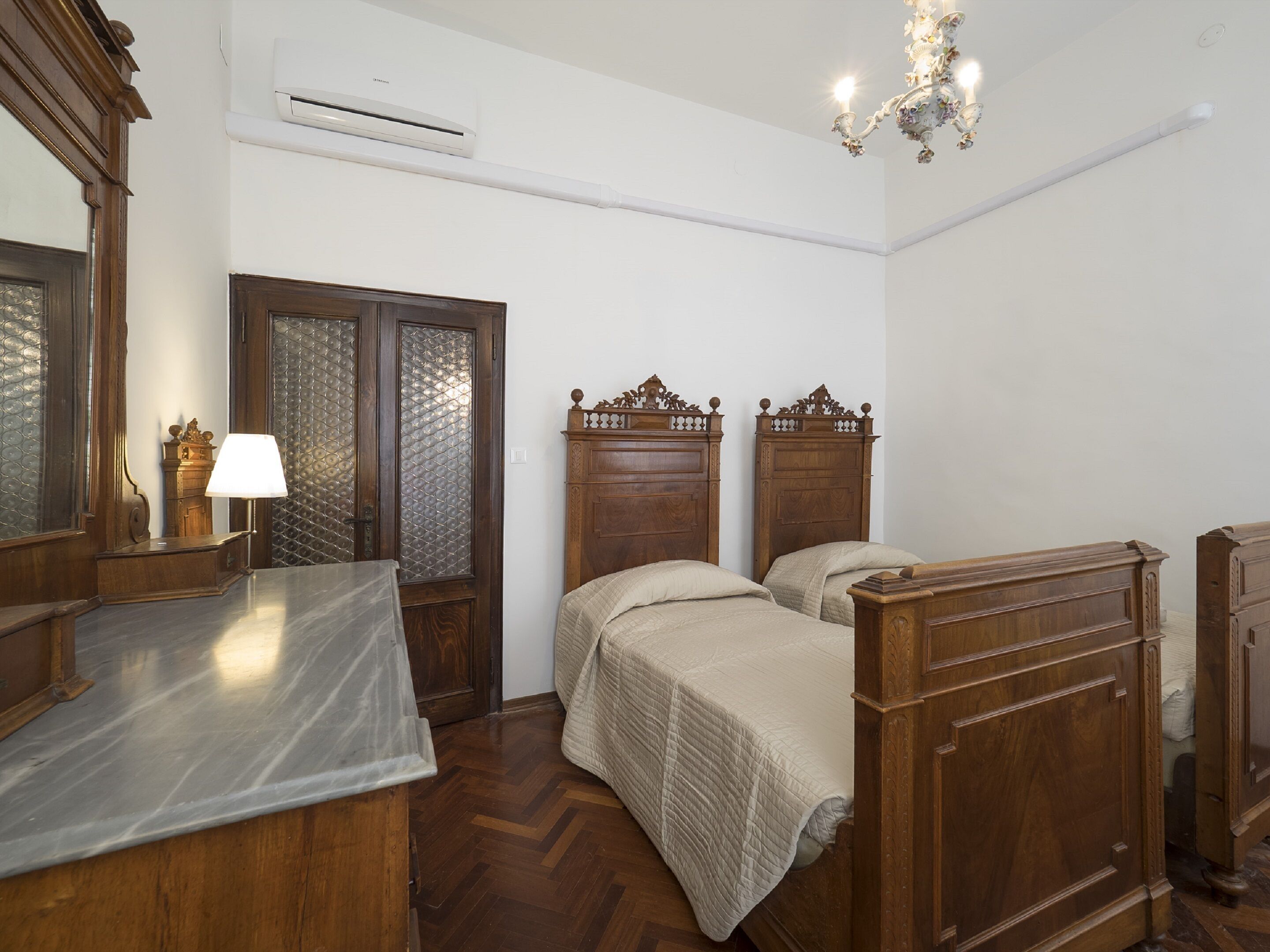 Un dormitorio con dos camas de madera, un tocador, una cómoda y una araña.
