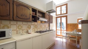 A kitchen with wooden cabinets, a stove, a microwave, and a sink. - San Marco Schiavoni Apartments (Venice)