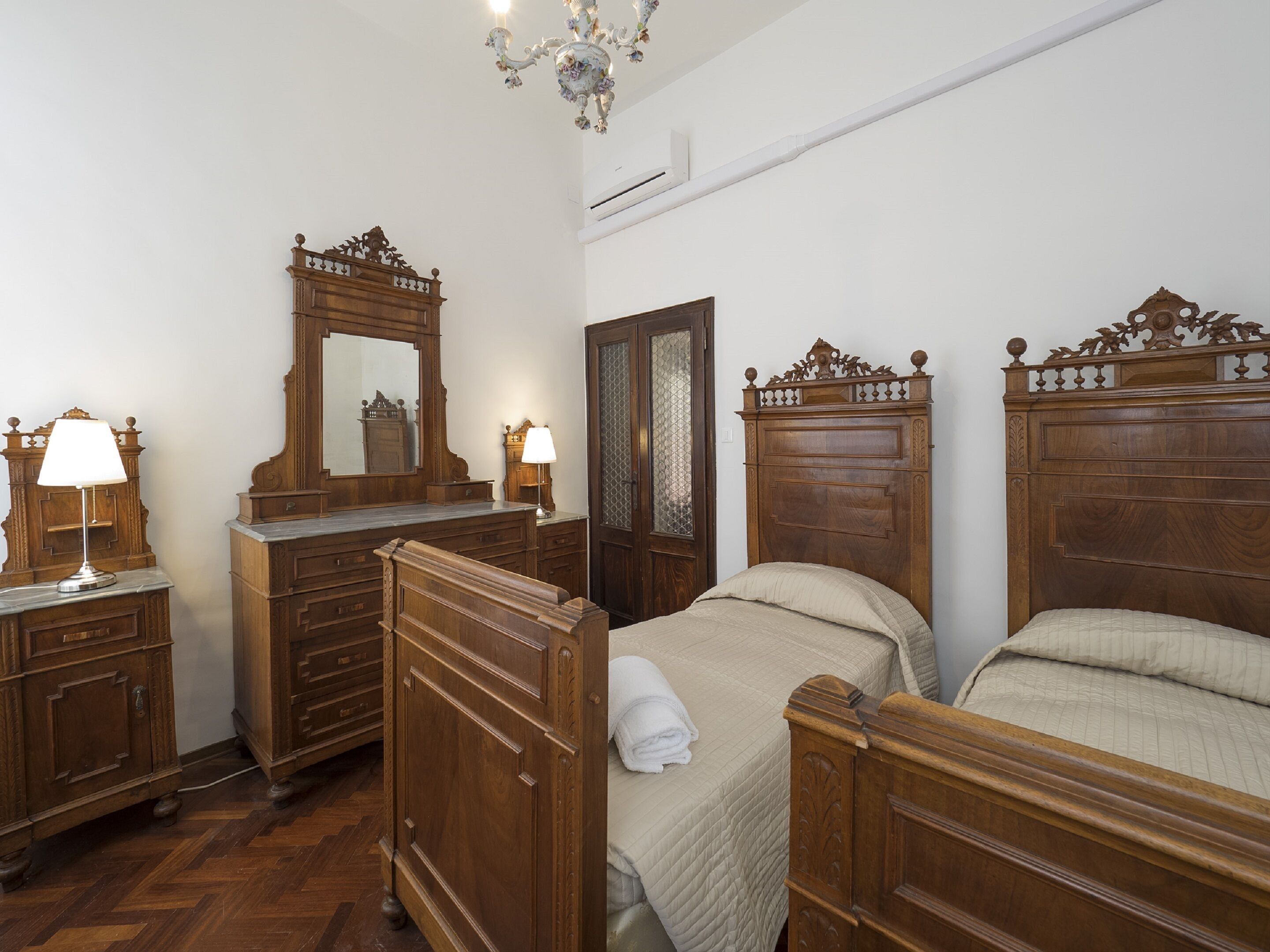 A bedroom with two wooden beds, a dresser, a mirror, and a chandelier.