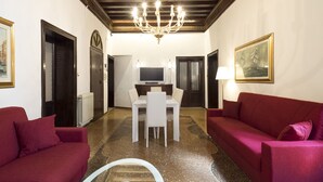 A living room with a chandelier, red sofas, a white table, and a TV. - San Marco Schiavoni Apartments (Venice)