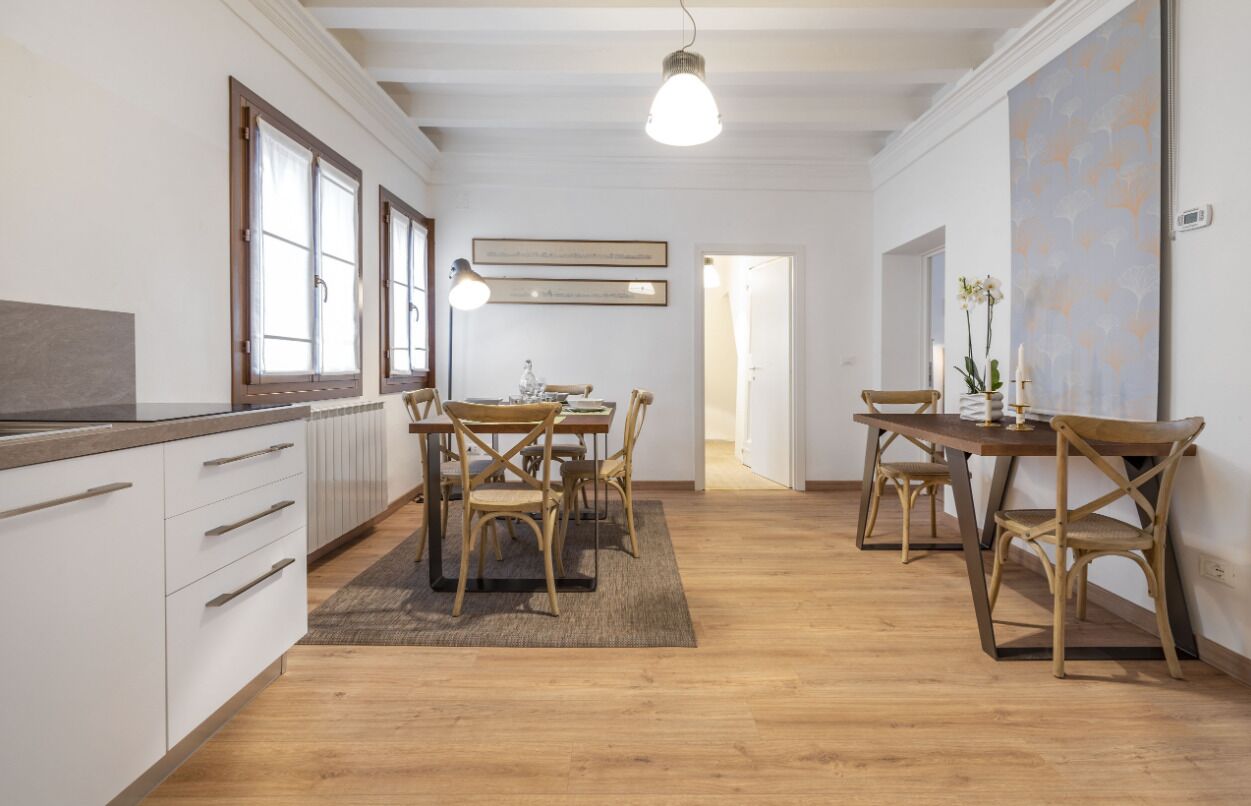 A modern kitchen with wooden cabinets, a dining table with chairs, and pendant lighting.