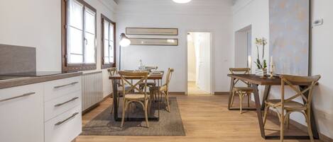 A modern kitchen with wooden cabinets, a dining table with chairs, and pendant lighting.