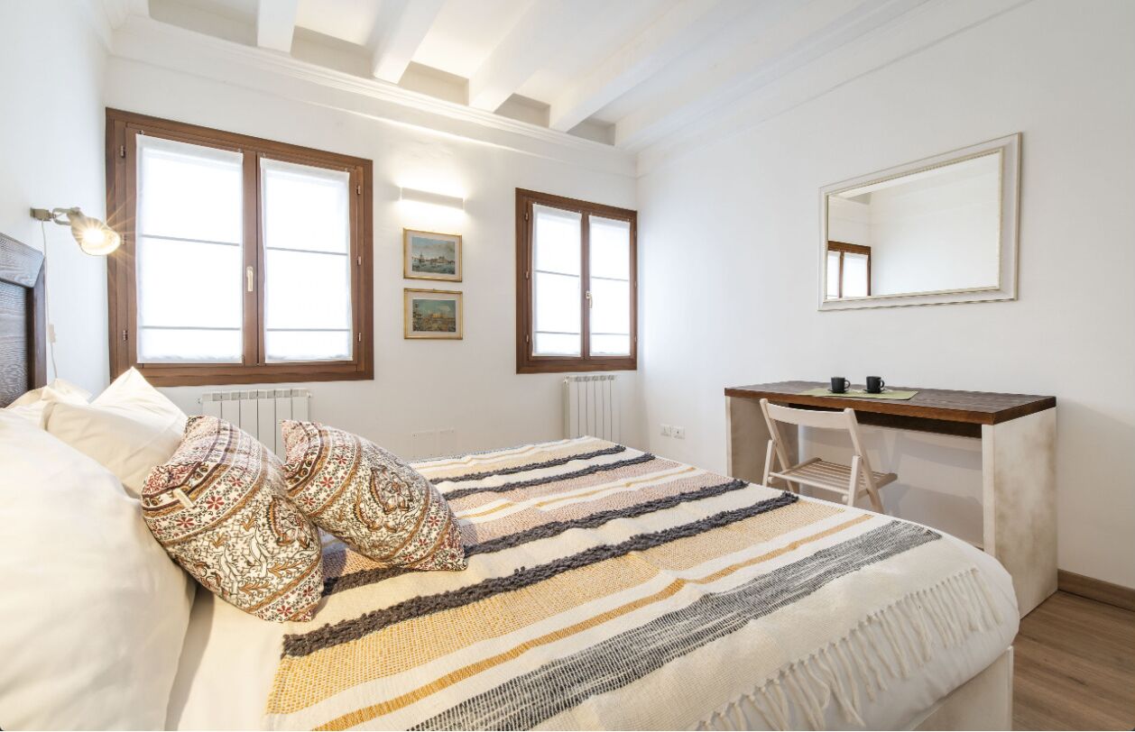 A bedroom with a bed, a desk, and a large window.