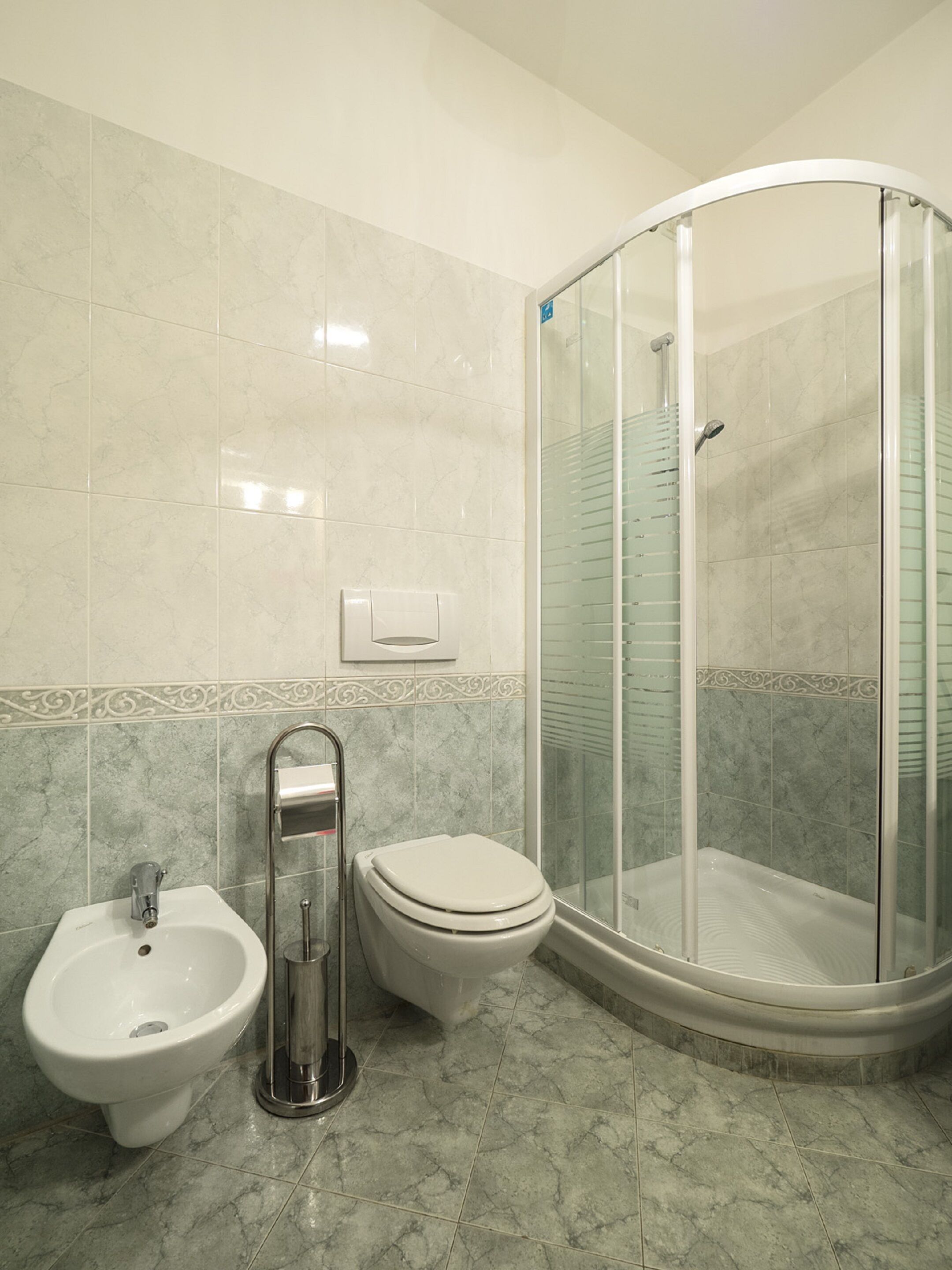 A bathroom with a bidet, toilet, and a glass-enclosed shower.