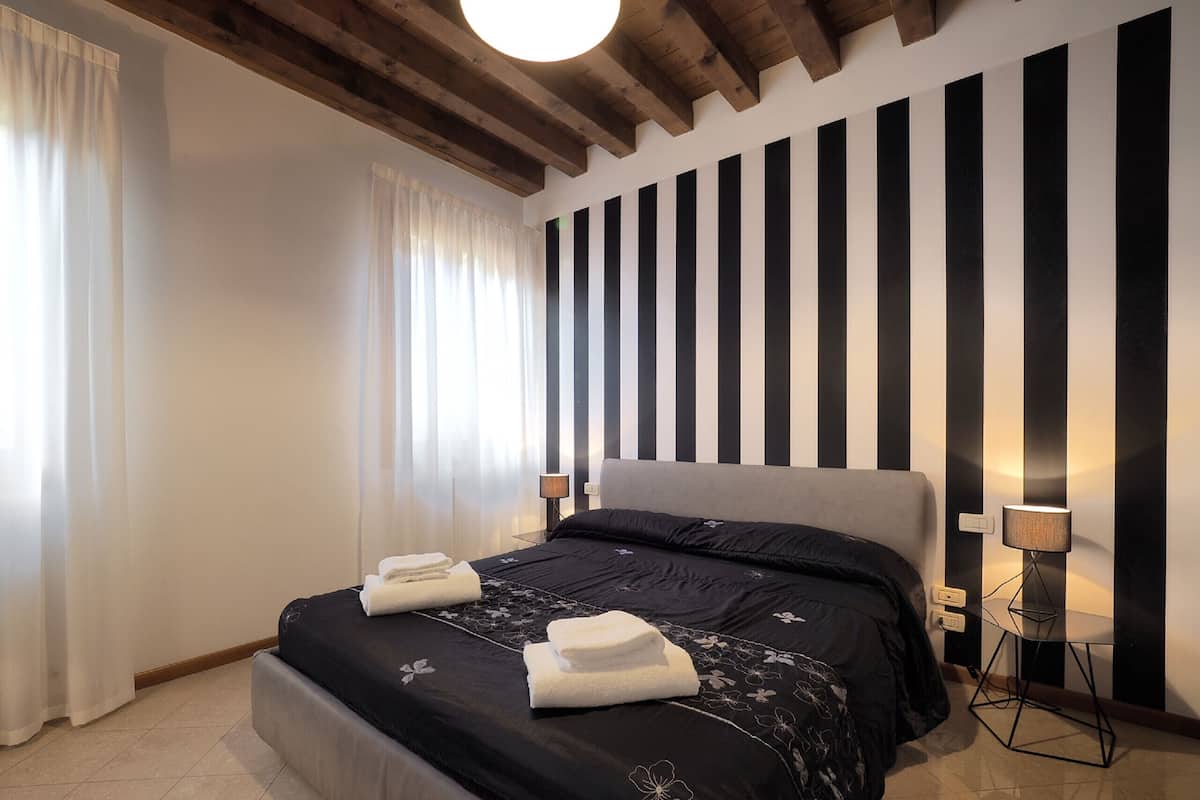 A modern bedroom with a large bed, two bedside lamps, and a striped wall.