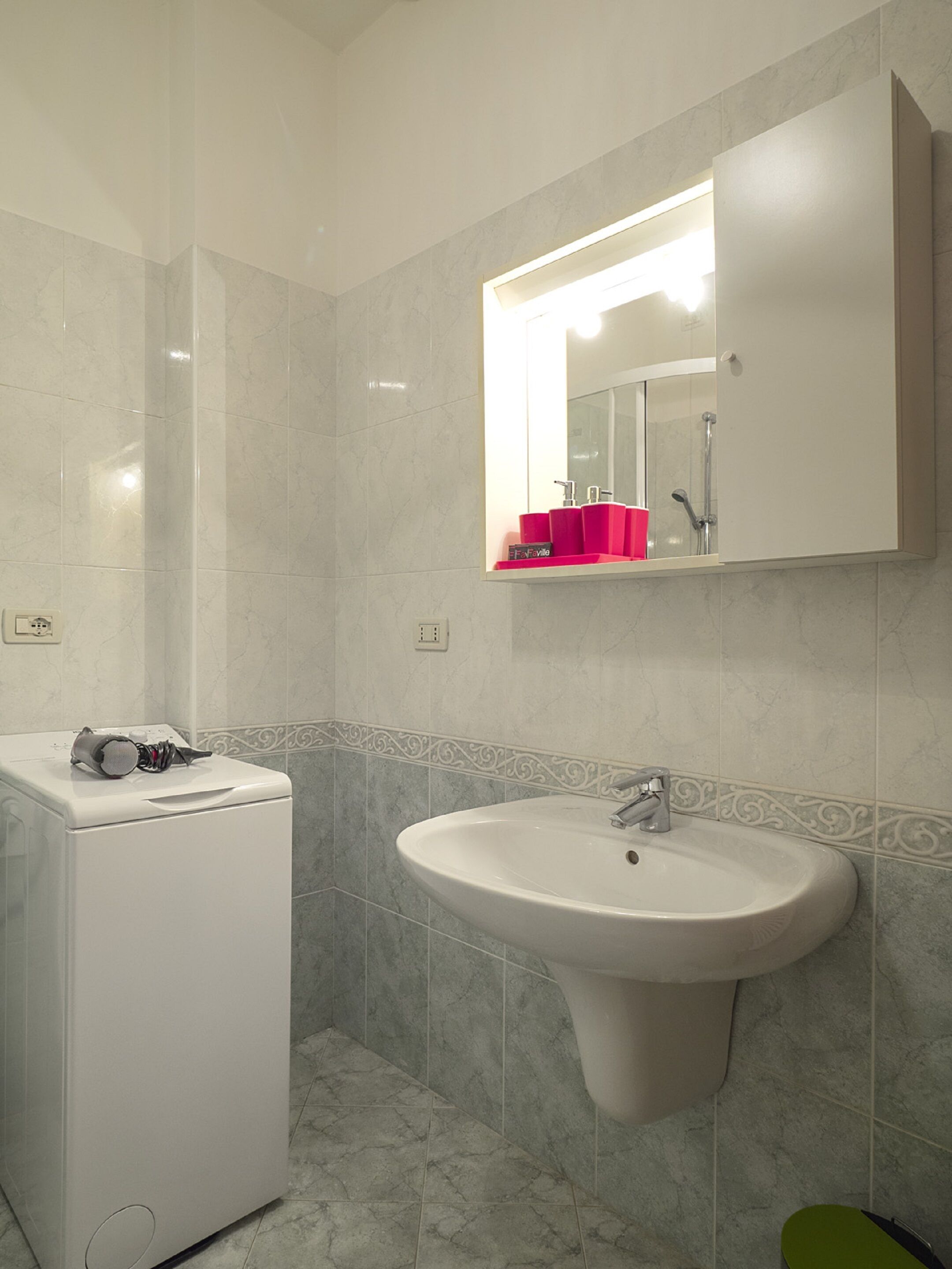 Un baño con un lavamanos blanco, un espejo encima y una lavadora a la izquierda.