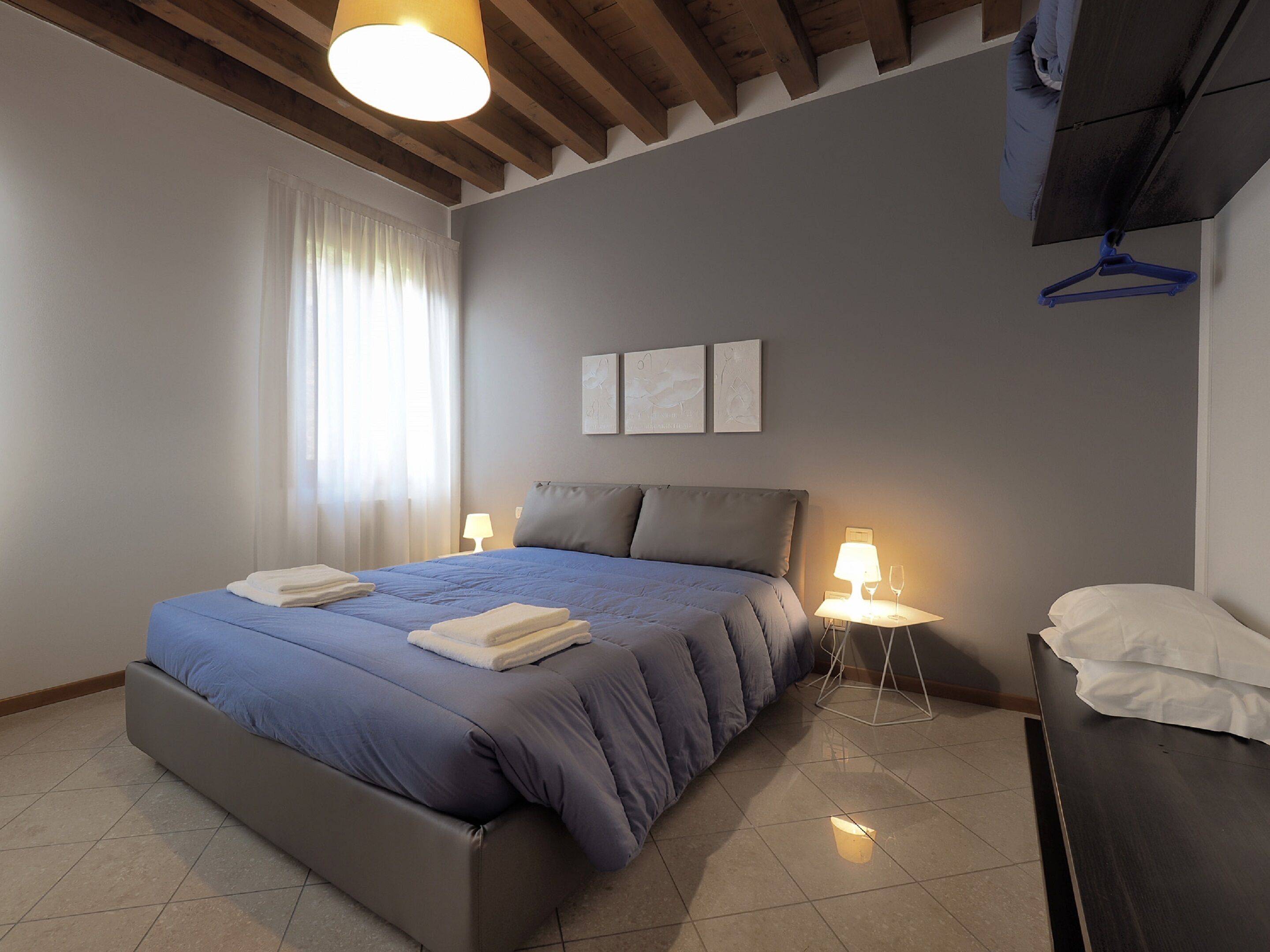 Un dormitorio con cama, lámparas de noche, una mesita de noche con un vaso y un perchero.