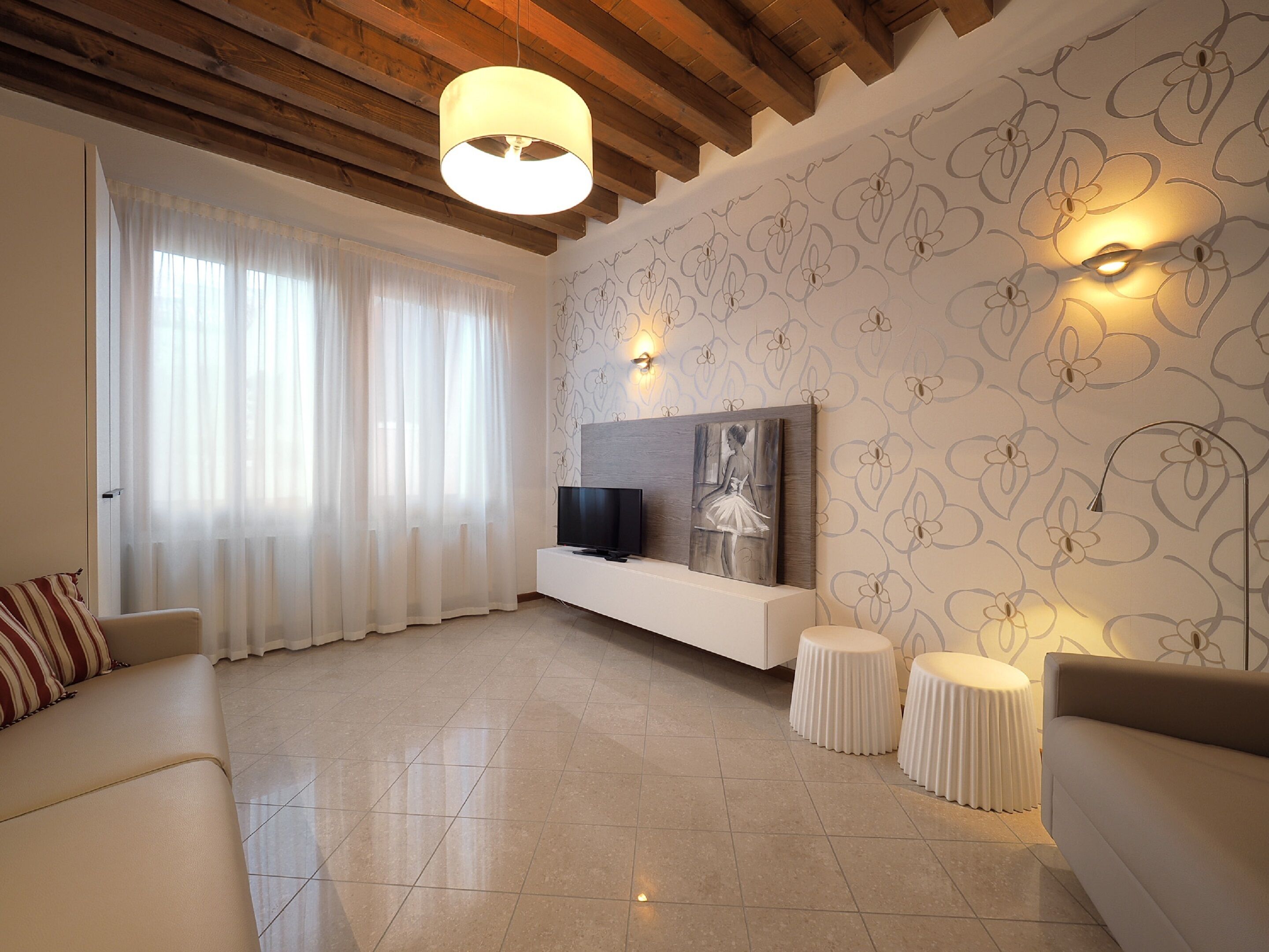 Una sala de estar moderna con techo de madera, un ventanal con cortinas translúcidas, un televisor de pantalla plana y un aplique de pared.