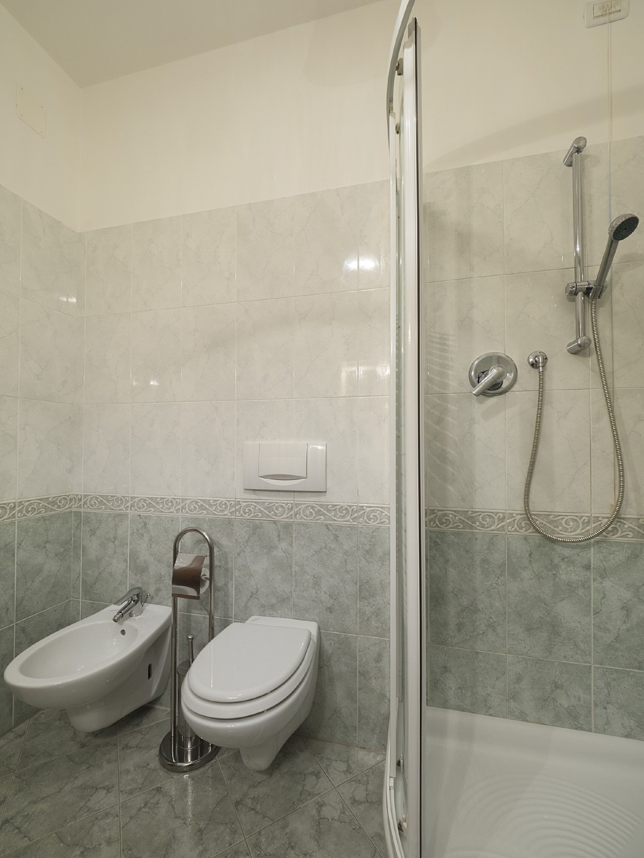 A bathroom with a shower, toilet, and bidet.
