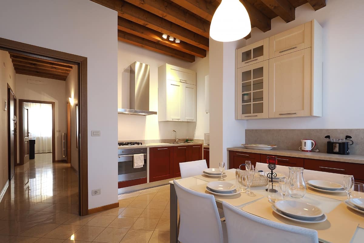 A modern kitchen with a dining area, featuring stainless steel appliances, wooden beams, and a large window.