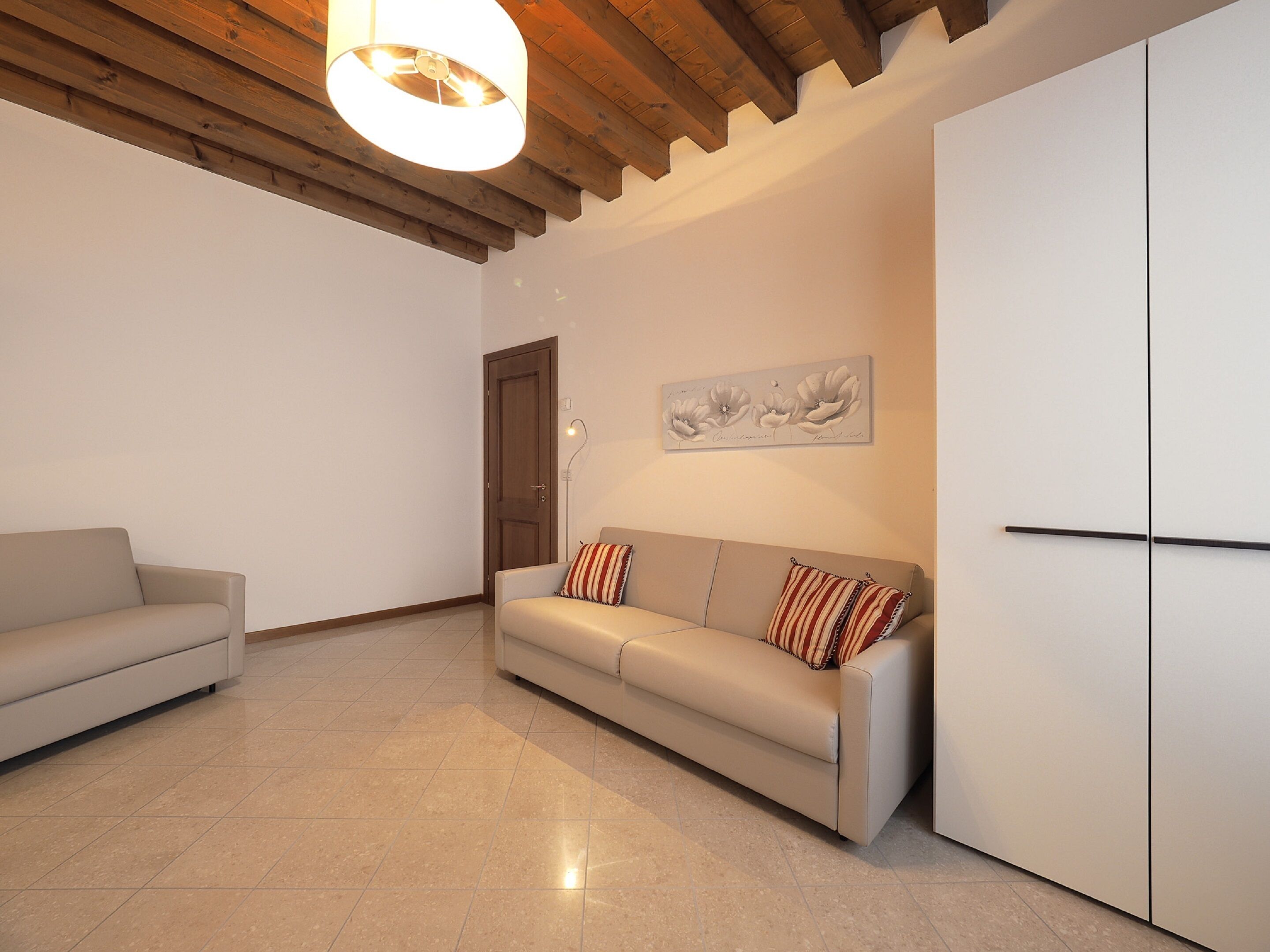 Un salon moderne avec un canapé beige, un plafond en bois, un mur blanc orné d’un tableau floral et un meuble blanc.