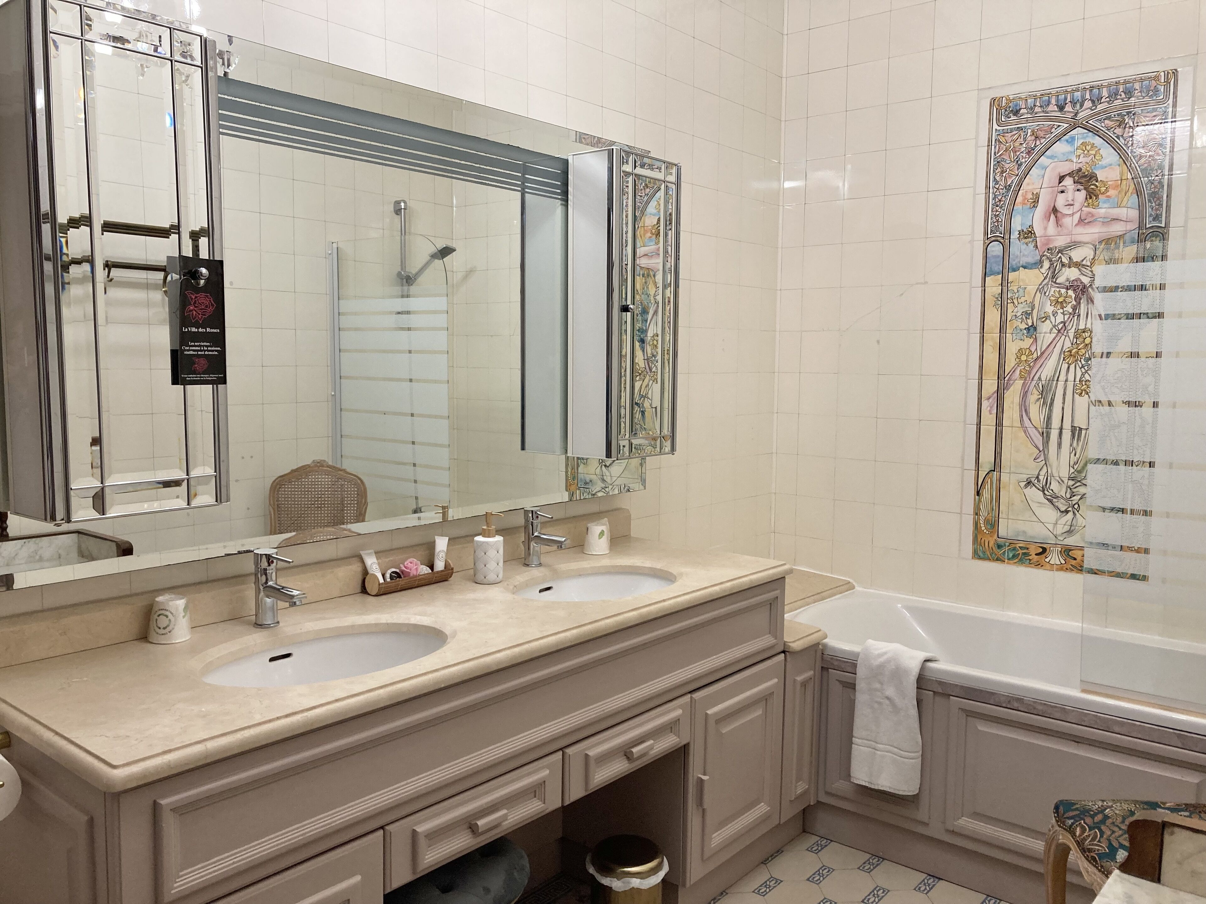 Un bagno con due lavandini, uno specchio grande, una vasca da bagno e un murale decorativo in ceramica.