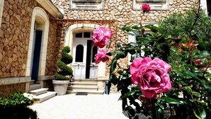 A stone building with a central entrance, steps leading up to it, and a small garden with pink flowers. - Villa des roses (Luçon)