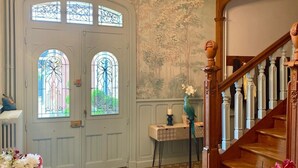 A grand entrance with a wooden staircase, a decorative door with stained glass windows, and a mural on the wall. - Villa des roses (Luçon)