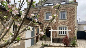A stone building with a cross, a paved courtyard, and flowering trees. - Villa des roses (Luçon)