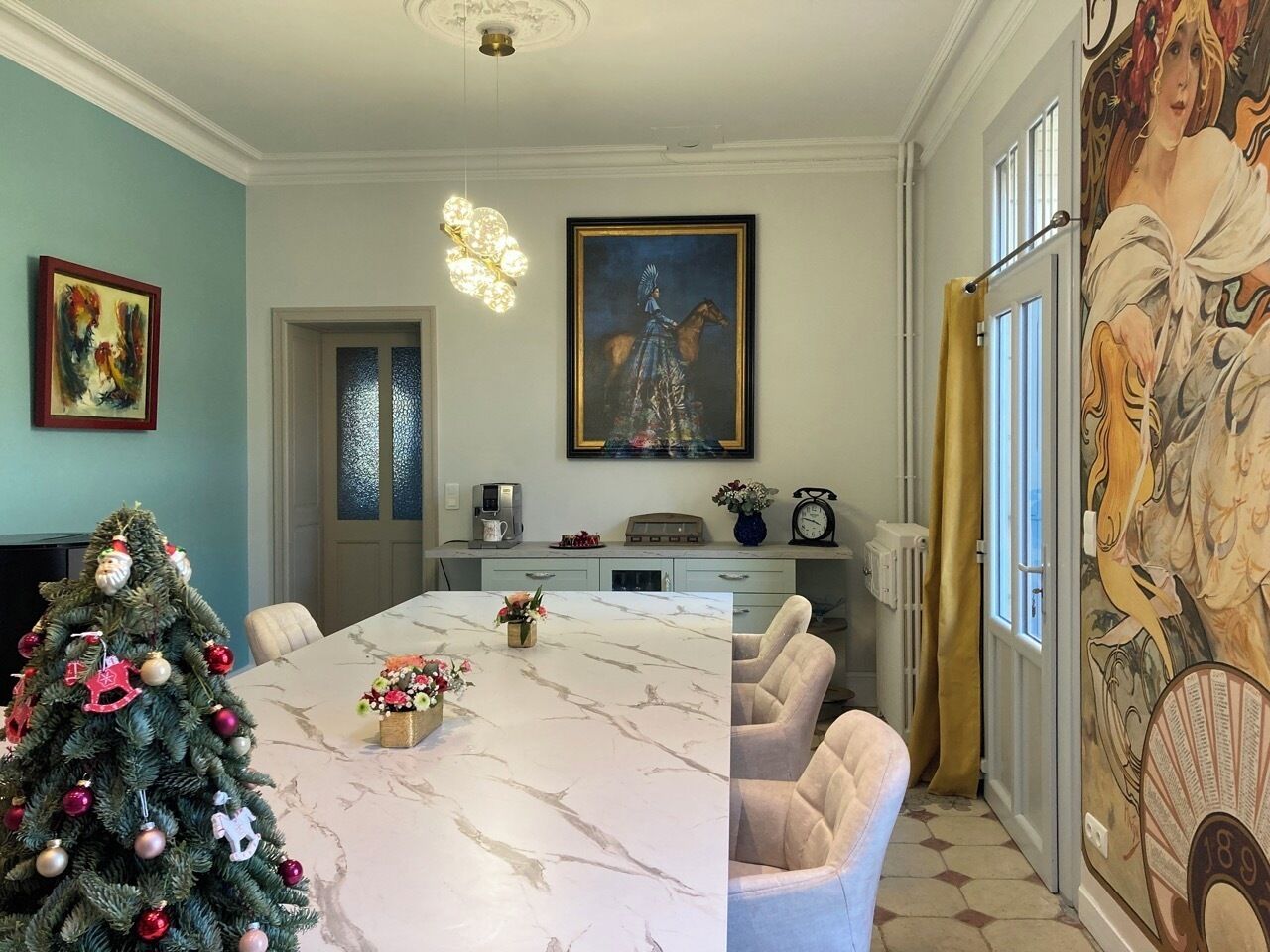 A dining area with a marble table, chairs, a Christmas tree, and a painting on the wall.