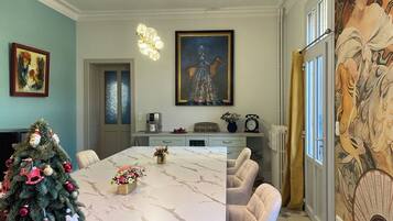 A dining area with a marble table, chairs, a Christmas tree, and a painting on the wall.