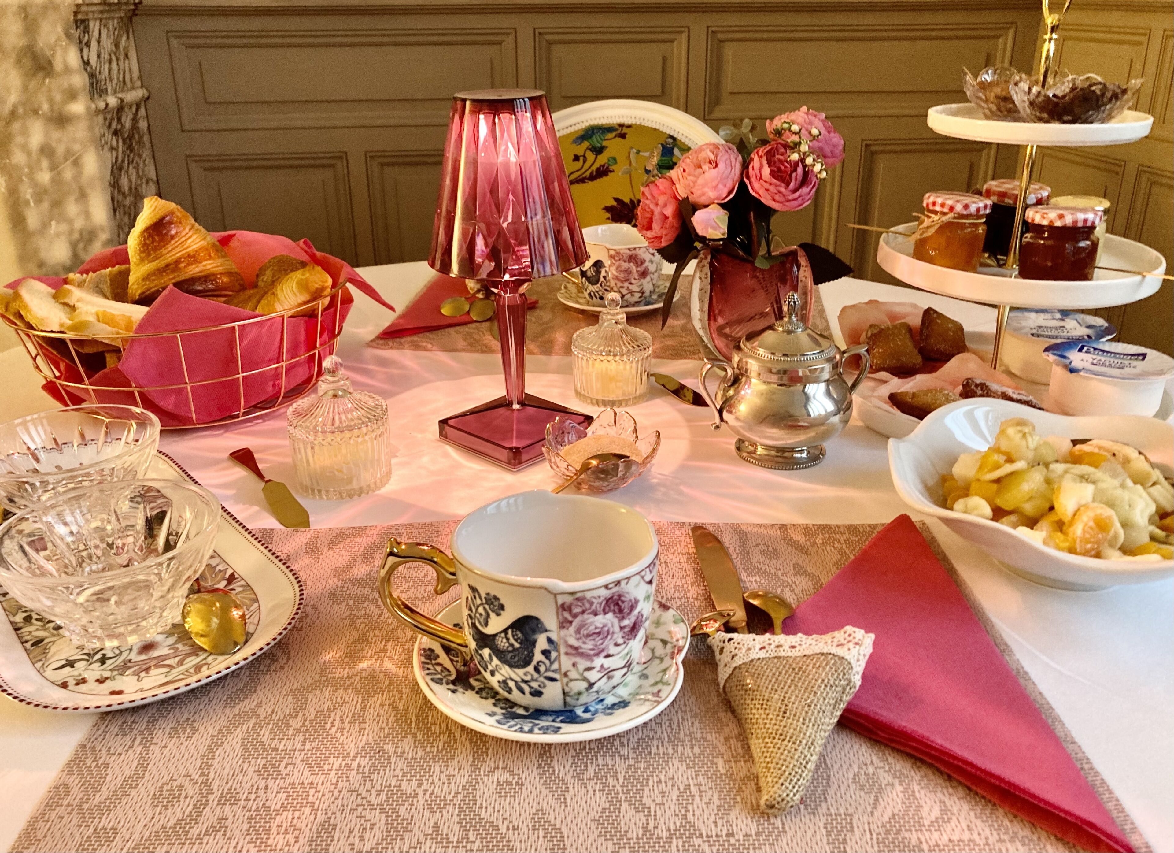 A table set with various items including a teapot, cups, a basket of bread, and a decorative lamp.