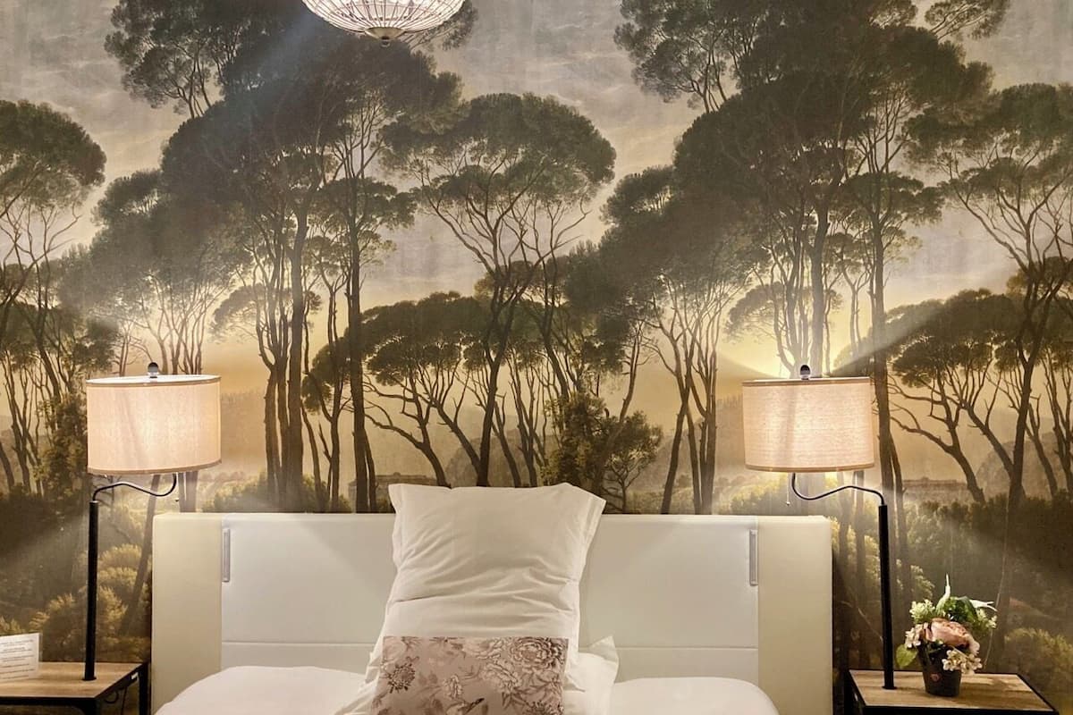 A bedroom with a large bed, two bedside lamps, and a forest-themed mural on the wall.