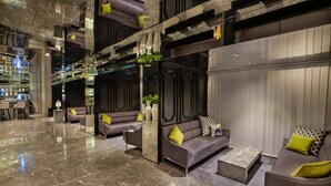 Um hall moderno com piso de mármore, sofás com almofadas, área de bar e um espelho grande que reflete o espaço.