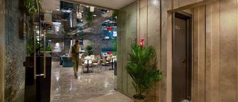 Eine moderne Lobby mit einer Glaswand, einer mit „WC“ beschrifteten Holztür und einem Blumentopf.