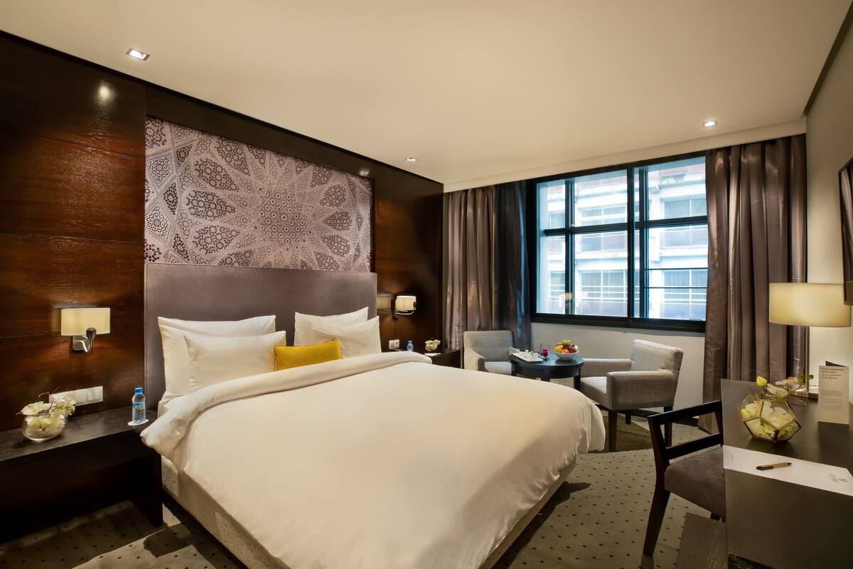 A hotel room with a large bed, a desk, a chair, and a window with curtains.