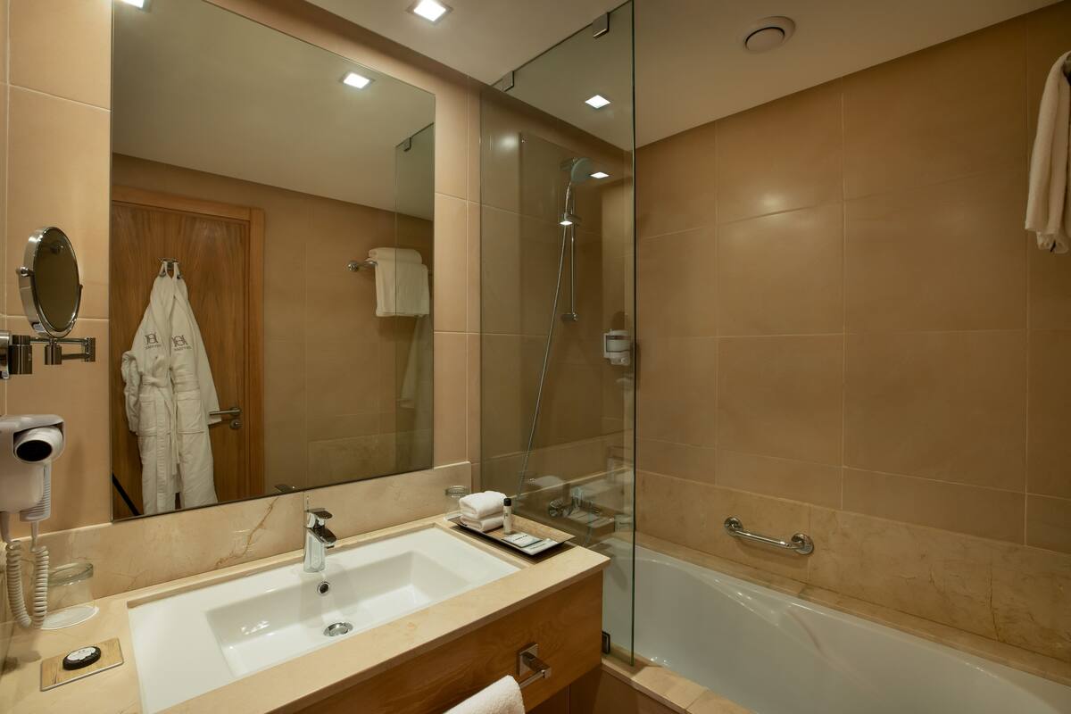 A modern bathroom with a large mirror, a sink, a glass-enclosed shower, and a bathtub.