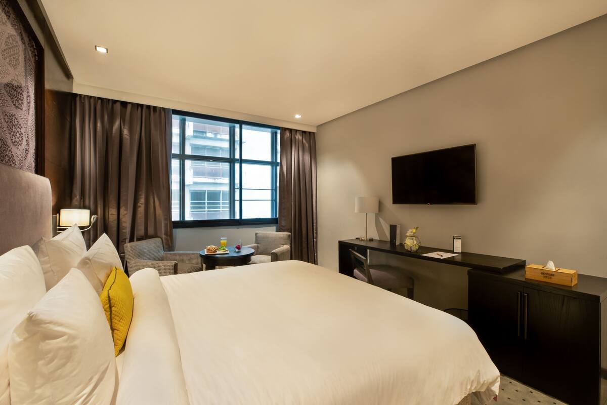 A hotel room with a large bed, a desk, a chair, a TV, and a window with curtains.