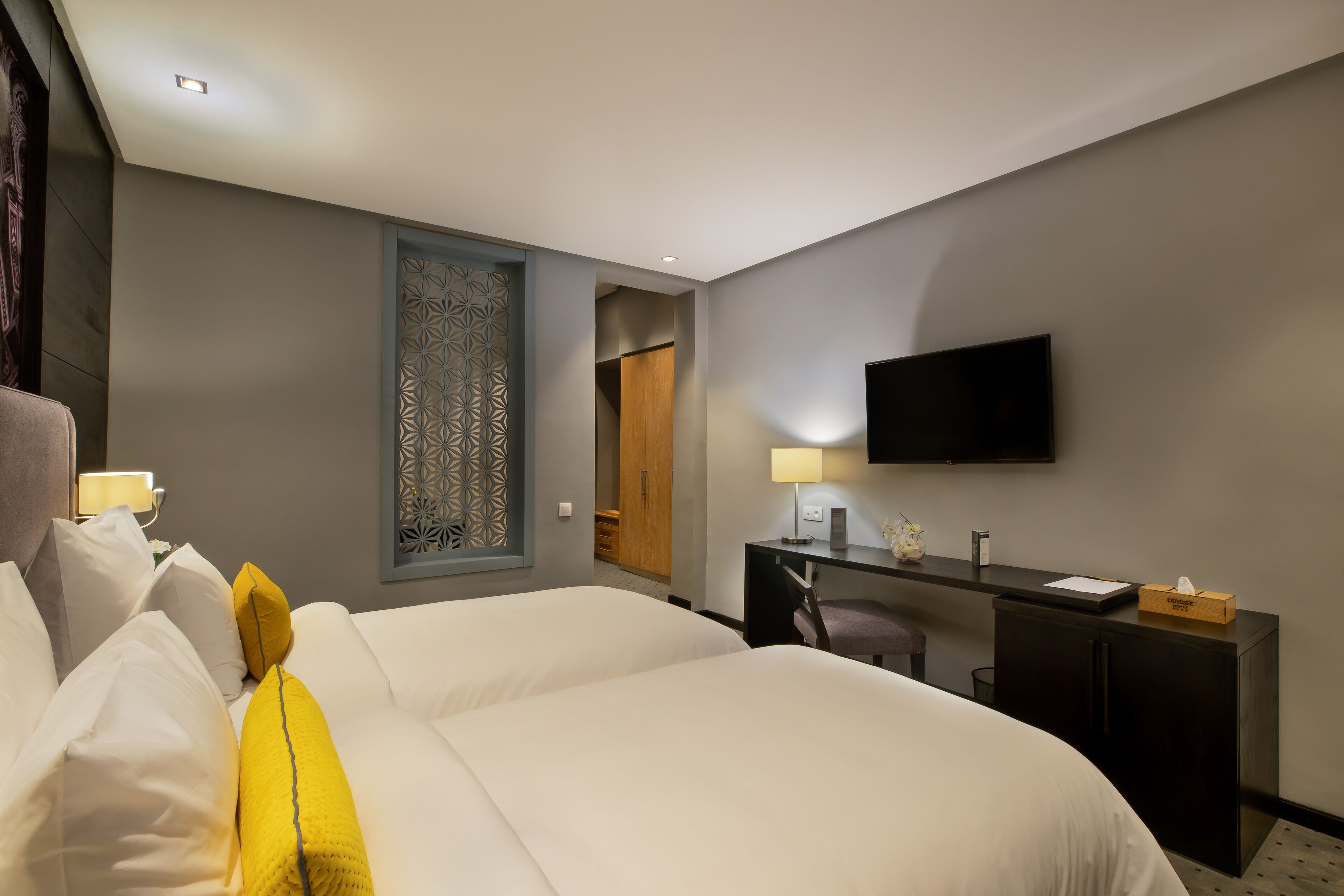 A hotel room with a large bed, a desk, a chair, a TV, and a wardrobe.