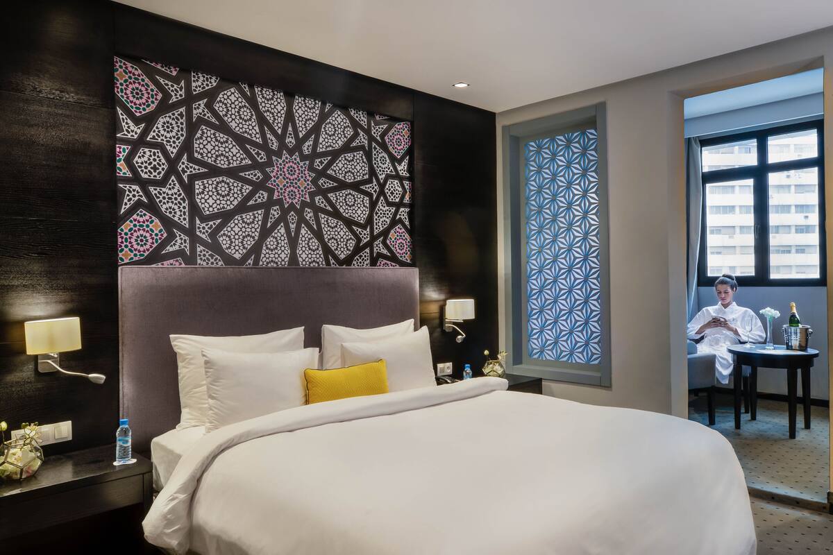A hotel room with a large bed, a nightstand with a lamp, a water bottle, and a decorative wall panel.