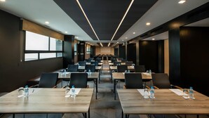 Sala de conferência com várias mesas e cadeiras, equipada com garrafas de água e placas de identificação.