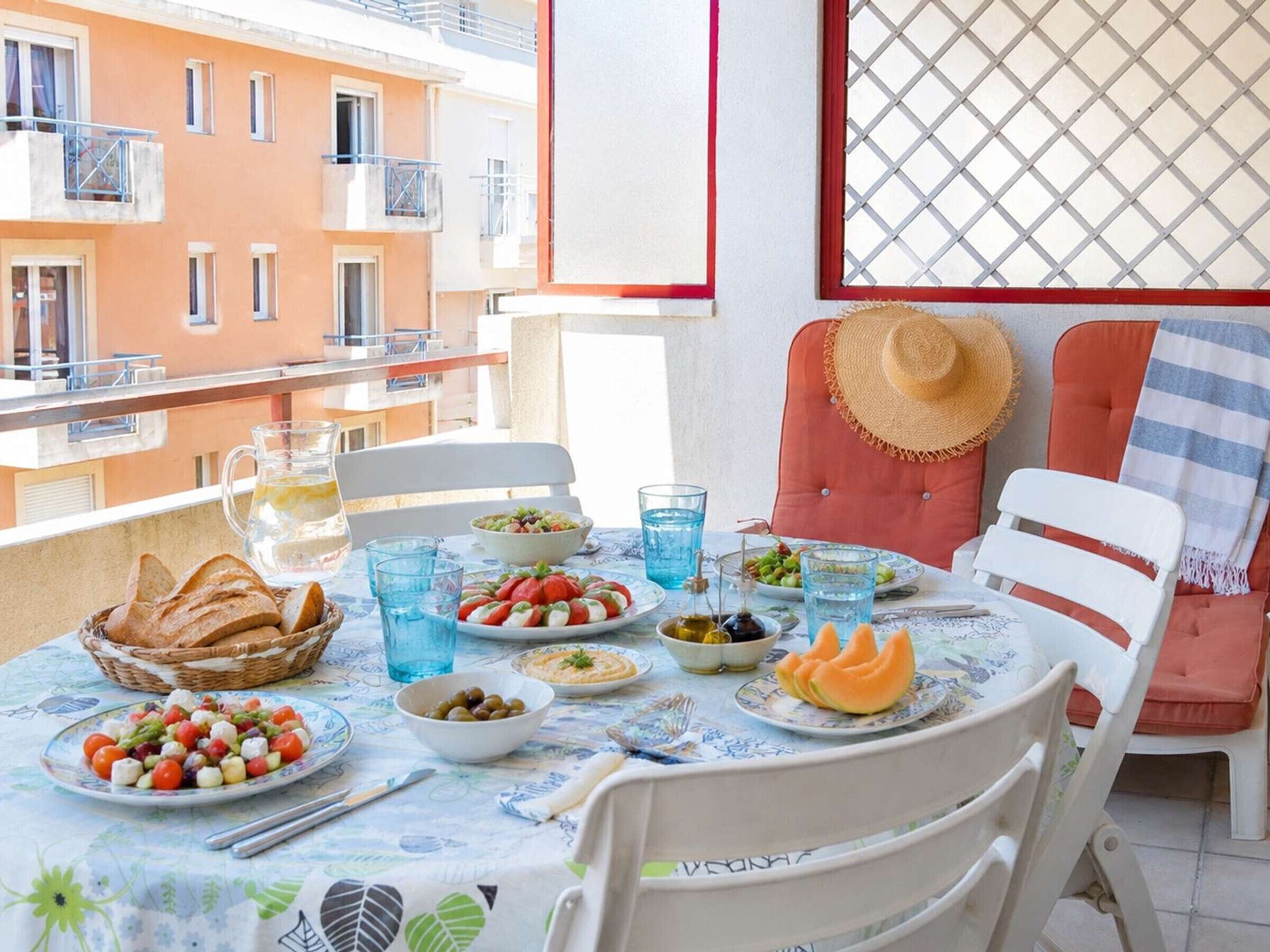Een balkon met een gedekte tafel, inclusief borden met eten, glazen en een mand met brood.