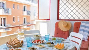 A balcony with a table set for a meal, including plates of food, glasses, and a basket of bread.