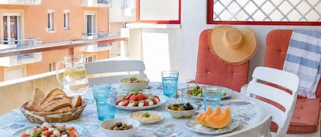 A balcony with a table set for a meal, including plates of food, glasses, and a basket of bread.