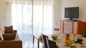 A living room with a sofa, a dining table with chairs, a television, and a cabinet.