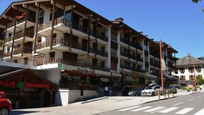 A multi-story building with balconies, a supermarket, and a restaurant. - Sunny 2BR Mezzanine Apt with Mountain Views, Fireplace, Near Shops & Lifts, Sleeps 6 (Le Grand-Bornand)