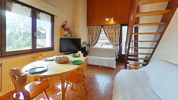 A cozy room with a wooden ceiling, a dining table with chairs, a bed, a TV, and a window with curtains. - Sunny 2BR Mezzanine Apt with Mountain Views, Fireplace, Near Shops & Lifts, Sleeps 6 (Le Grand-Bornand)